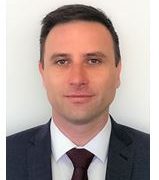 A professional headshot of a man wearing a suit and tie, presenting a friendly and approachable appearance, likely for a business profile.