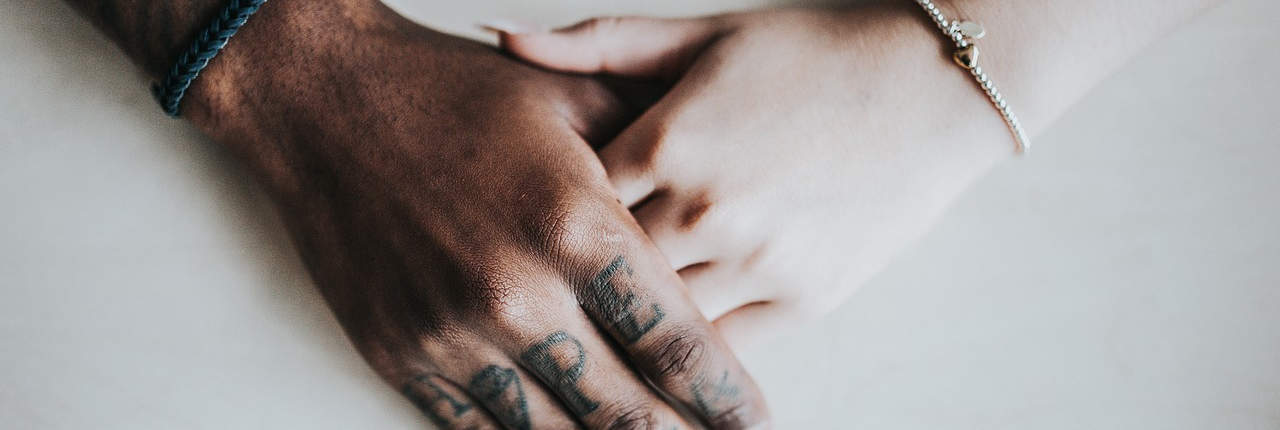 Close-up image of two hands clasped together, one with the word 'HOPE' tattooed on the fingers, symbolizing support, unity, and optimism