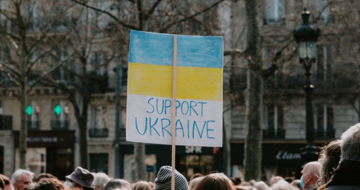 An image capturing a protest sign with the words "Support Ukraine" painted over the colors of the Ukrainian flag, representing solidarity and political activism.