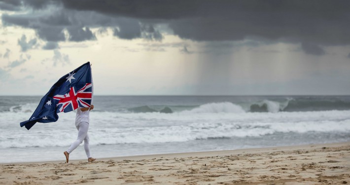 A person draped in the Australian flag stands on a stormy beach, capturing a patriotic moment or celebrating national pride.