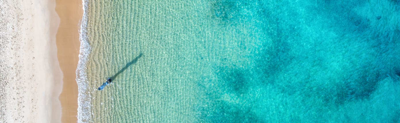 A top-down view of a white sand beach beside clear blue waters