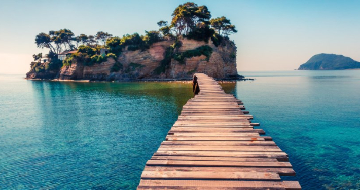 A wood plank bridge stretching from shore to a small tropical island