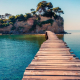 A wood plank bridge stretching from shore to a small tropical island