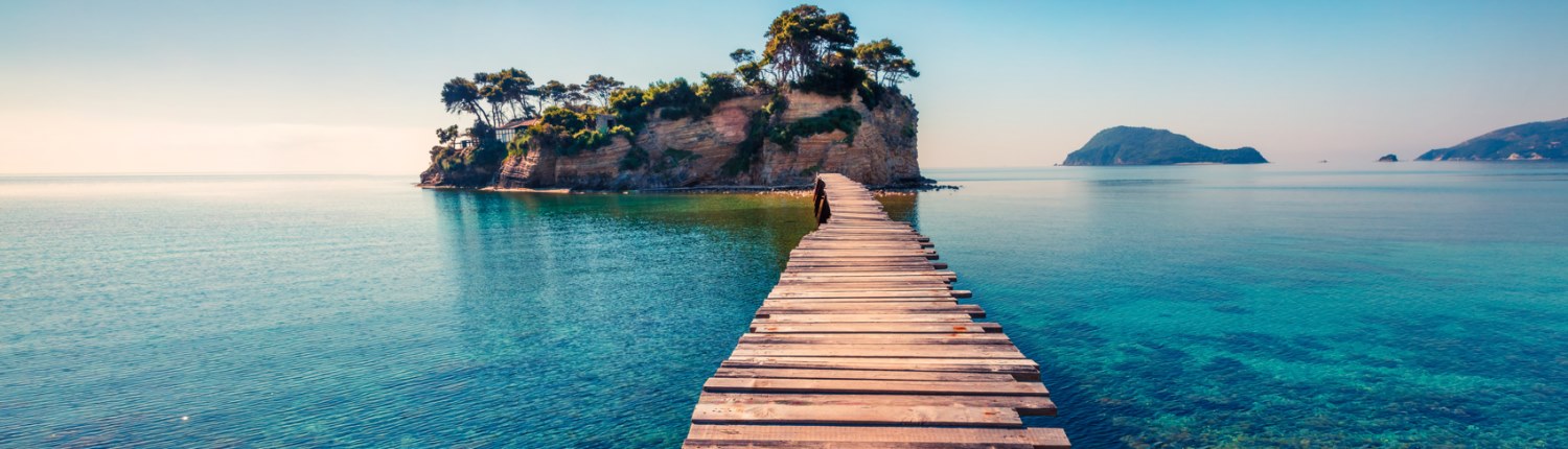 A wood plank bridge stretching from shore to a small tropical island