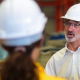 A group of workers wearing hard hats have a meeting in a warehouse