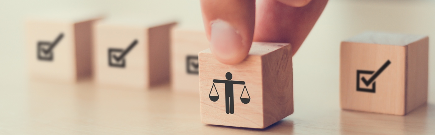 A small wooden block with a simple illustration of a person balancing weights like scales, suggesting justice