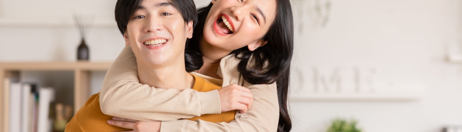 A women hugs her seated partner from behind, both smiling